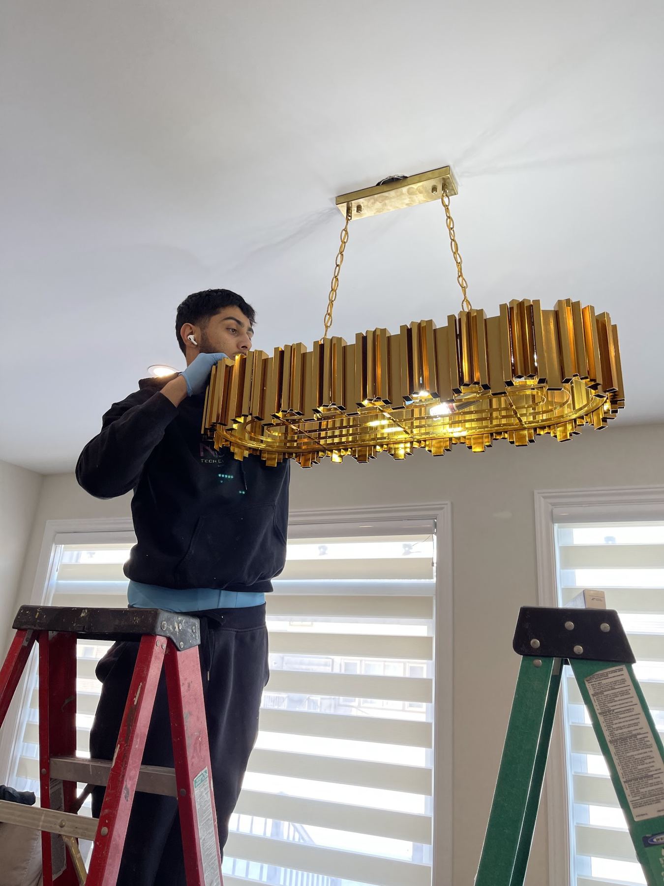 Moe on a ladder hanging a gold chandelier